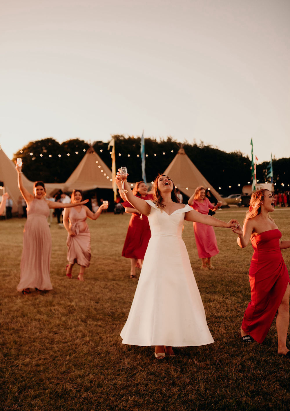Bride with bridesmaids dancing in front of wedding tipis